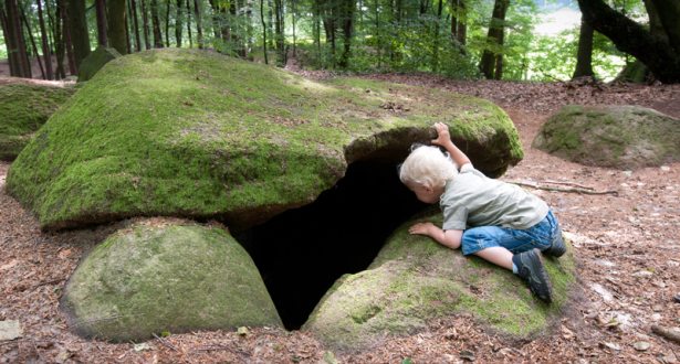 Ein kleiner Junge schaut hinunter in die dunkle Höhle eines Steingrabs