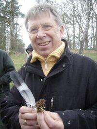 Jürgen Persiel hält eine Feder und ein Stück Heidepflanze in der Hand